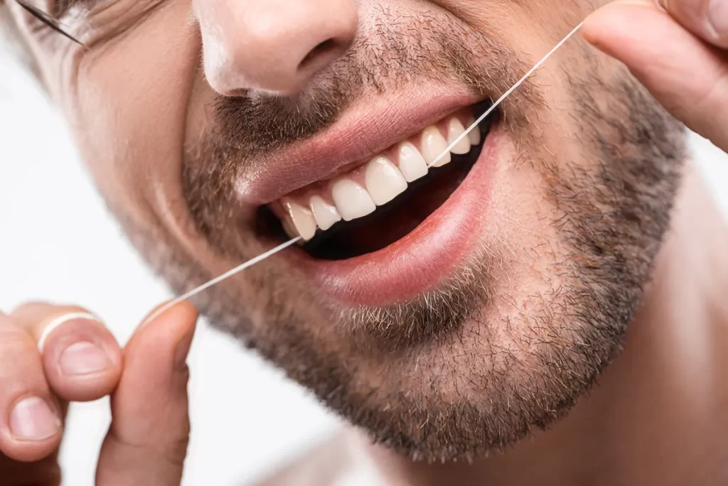 Smiling person holding floss behind their teeth.
