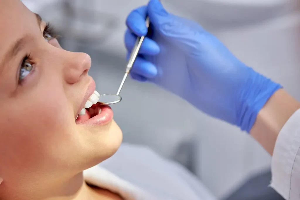 child smiling as dentist inspects teeth with a mirror