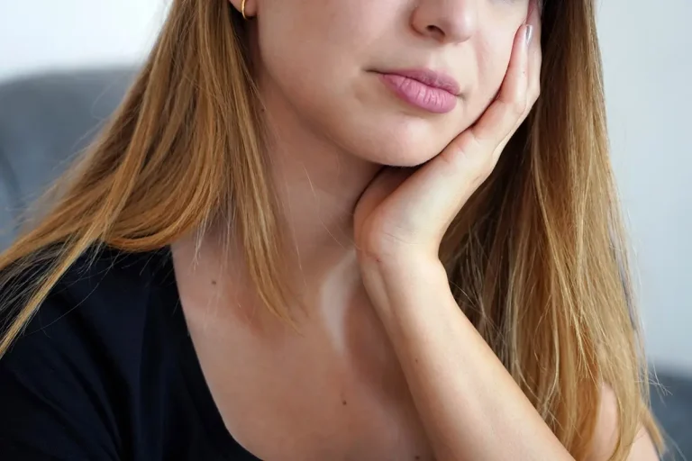 Bottom half of woman with long hairs face holding their hand to the side of their face. Looking like they are in pain.