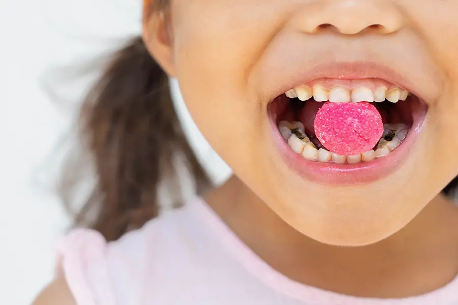 Young girl eating pink candy with cavities visible in teeth